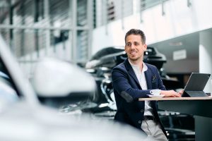 Geschäftsmann mit Tablet und Kaffee in einem modernen Autohaus, Businessfotos Köln