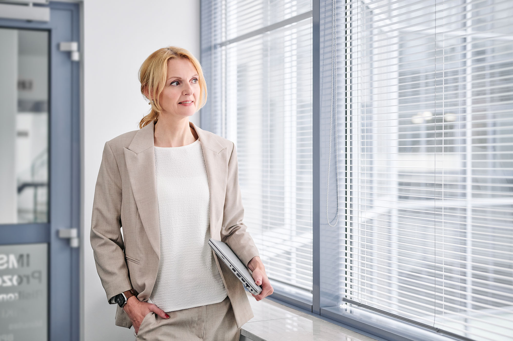 BBusinessportrait einer Geschäftsfrau mit Laptop am Bürofenster, Unternehmensfotografie Köln