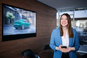 Mitarbeiterin im modernen Porsche Showroom mit Smartphone