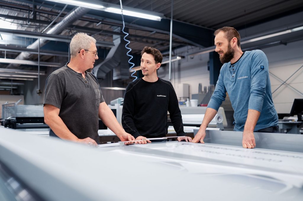 Drei Männer stehen in einer Industriehalle und besprechen sich