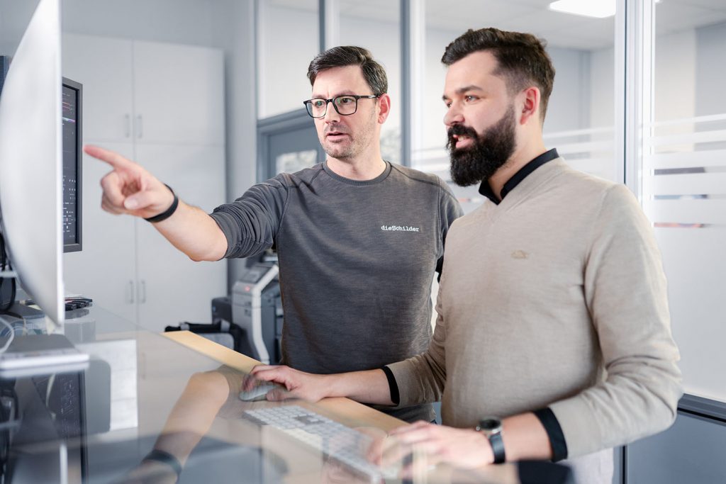Zwei Männer stehen in einem Büro vor einem Bildschirm