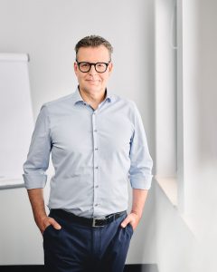 Mitarbeiterfoto eines Geschäftsführers im Hemd am Fenster