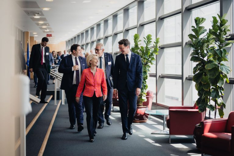 EU-Kommissionspräsidentin Ursula von der Leyen und NRW-Ministerpräsident Hendrik Wüst gehen durch einen hellen Flur und unterhalten sich.