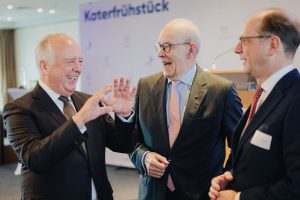 Drei Geschäftsleute unterhalten sich lachend beim Netzwerken auf einer Veranstaltung in Köln